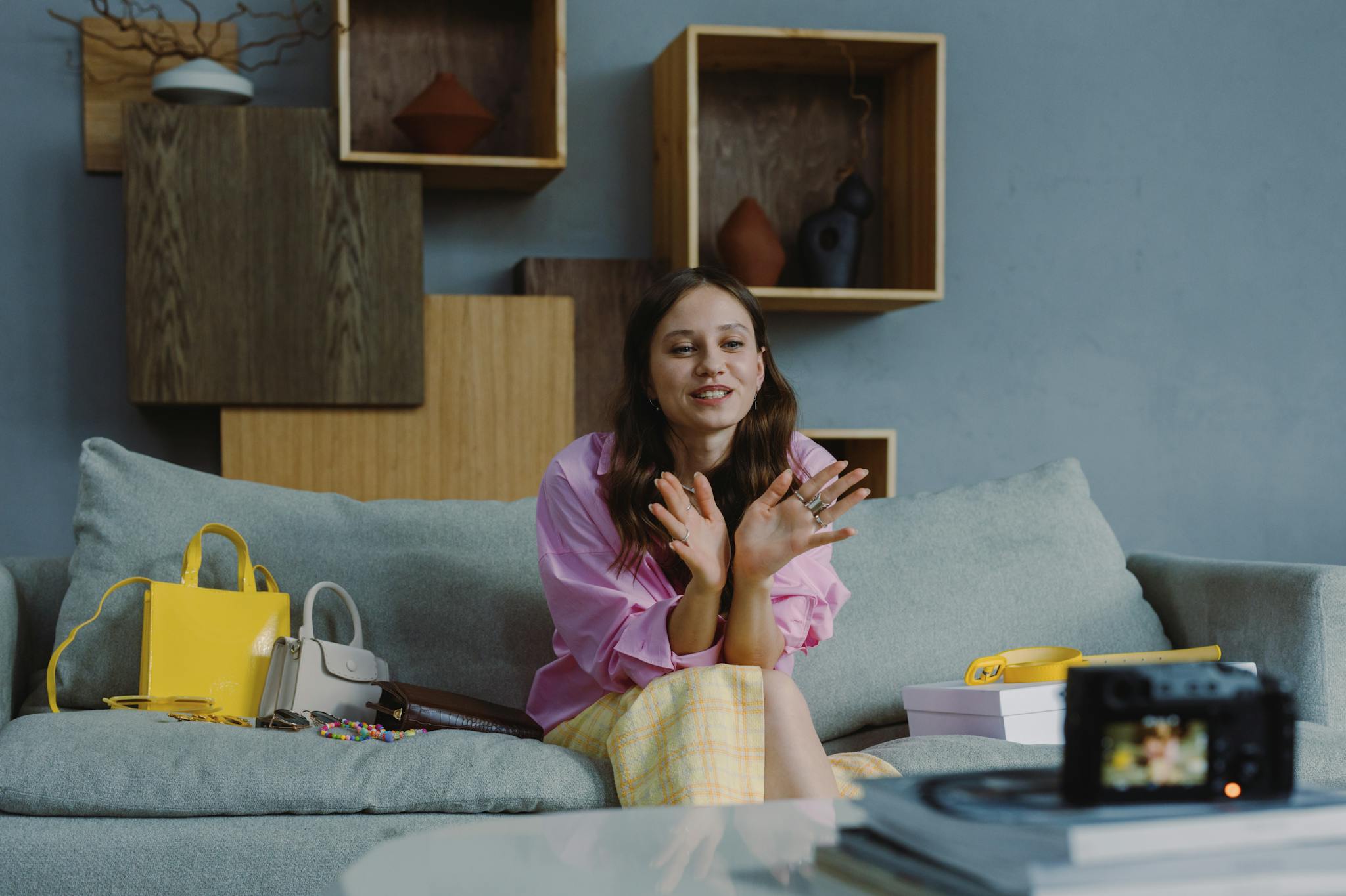 Young woman sitting on a couch, recording a fashion video blog indoors with stylish accessories and camera.